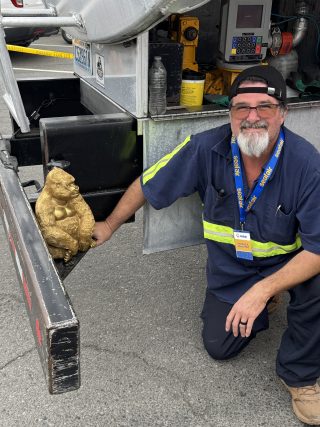 Snyder Green employee in uniform kneeling beside a golden gorilla statue.